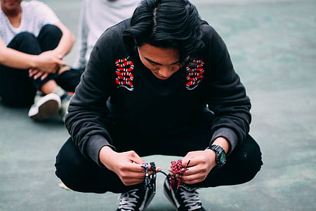 man squatting on gray pavement with black sitting nearby thumbnail