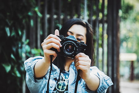 woman wearing blue chambray jacket holding black Canon DSLR camera thumbnail