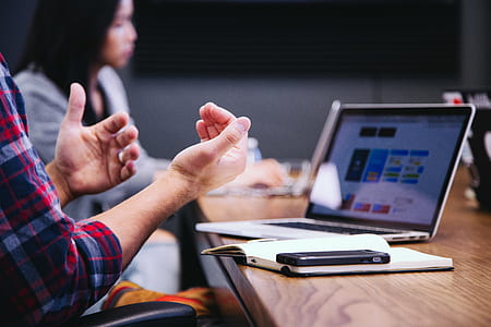 selective focus photography of person in red shirt doing hand gesture in front of brown table thumbnail