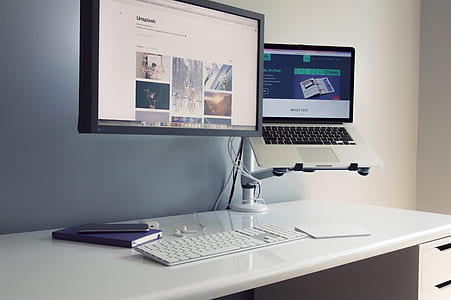 flat screen monitor near MacBook on white wooden desk thumbnail