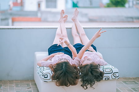 two women in pink shirt and blue shorts leaning on white textile at daytime thumbnail