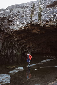 boy standing on rock surrounded by body of water near under white sky during daytime thumbnail