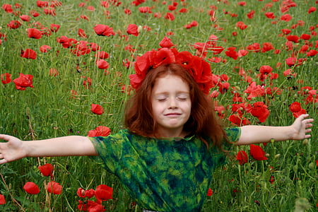 girl in green and black shirt standing on red petaled flowers field thumbnail