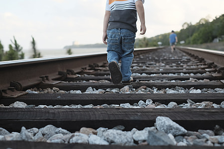 toddler walking on train rail during daytime thumbnail