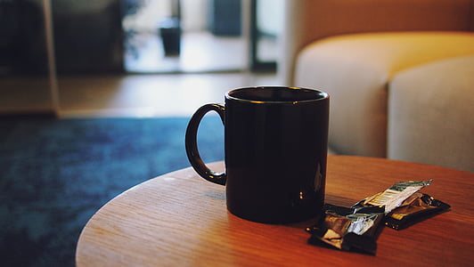 black ceramic mug placed on brown wooden coffee table selective focal photo thumbnail