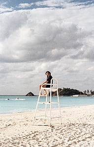 man sitting on lifeguard chair on seashore thumbnail