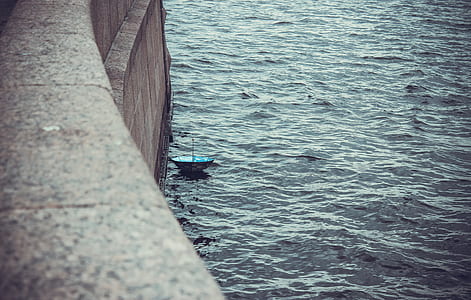 black and blue umbrella on body of water near concrete wall thumbnail