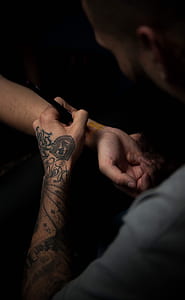 man in gray shirt doing henna tattoo on person's right wrist thumbnail