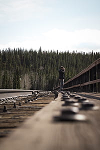 man standing on railroad taking picture near trees during day thumbnail