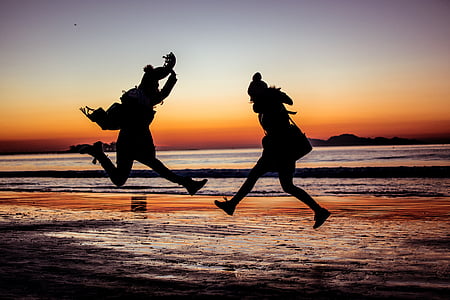 silhouette photo of two person jumping beside body of water thumbnail