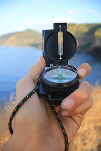 person holding black compass in front of ocean water during daytime shallow focus photography thumbnail
