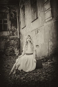 grayscale photo of woman sitting on rock near wall thumbnail