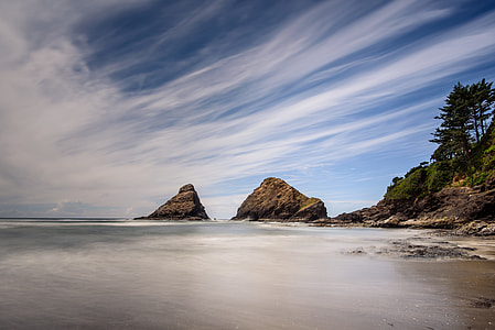 boulders on seashore under blue and white sky thumbnail