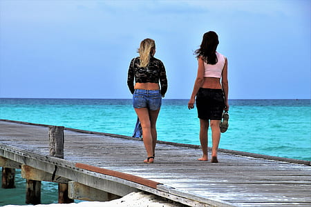 two women walking on boardwalk during daytime thumbnail