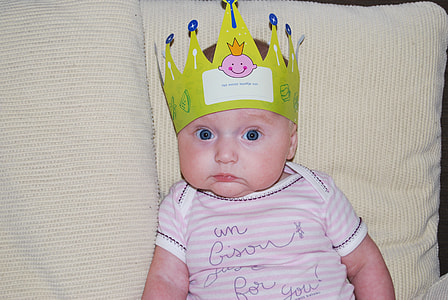 baby's wearing white and pink stripe onesie and green crown sitting in sofa thumbnail