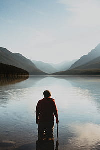 man standing on body of water facing mountain at daytime thumbnail