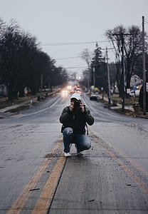 man sitting in middle of road while taking photo thumbnail