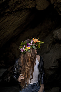 woman in black leather biker jacket with yellow hibiscus flower headdress standing near grey making post during daytime thumbnail