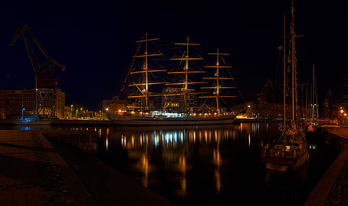 brown galleon ship near sailboats during nighttime thumbnail