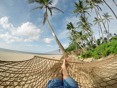 person with blue shorts lying on brown mesh hammock on seashore with blue sky and white clouds during daytime close-up photography thumbnail