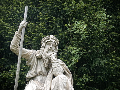 man holding stick statue near tree thumbnail