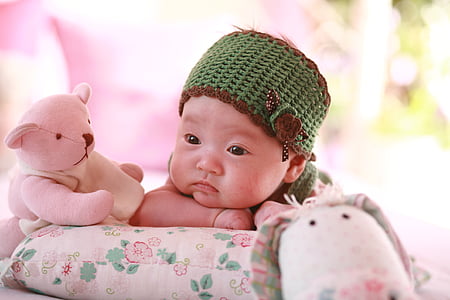baby wearing green and brown knitted cap near pink teddy bear thumbnail