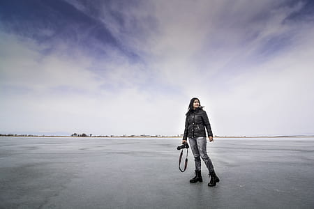 woman standing on grey pavement holding camera thumbnail