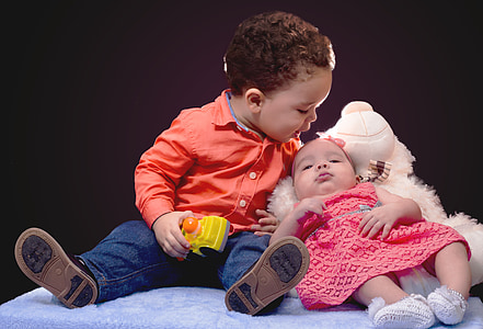 boy holding toy sitting near lying baby thumbnail