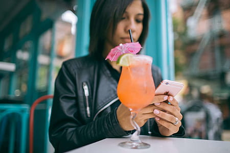 Woman Holding Mobile Phone with a Cocktail Glass on the Table thumbnail