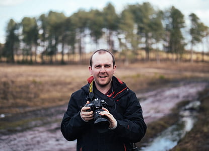 selective focus photography of standing man holding DSLR camera with lanyard thumbnail