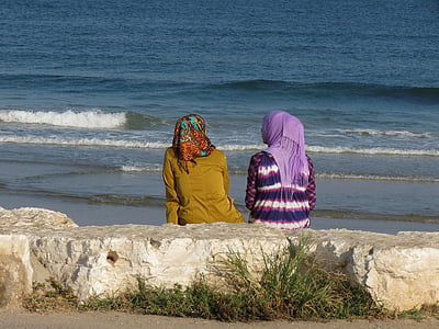 two women sitting beside seashore thumbnail