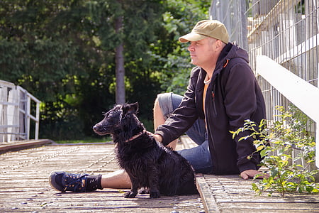 man sitting on curb beside black dog during daytime thumbnail