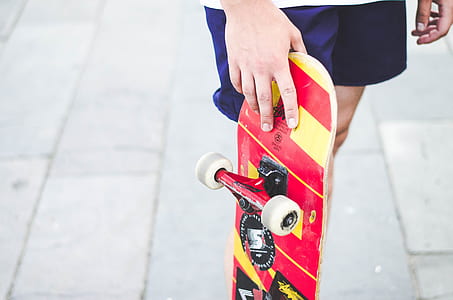 person holding red and yellow skateboard thumbnail