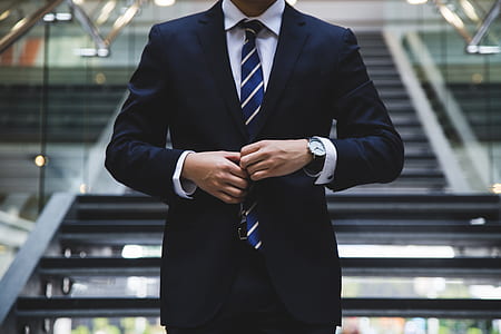 man in front of grey staircase unbuttoning his black suit jacket thumbnail