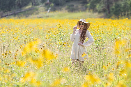 woman in white long-sleeved dress and hat standing in field of yellow flowers thumbnail