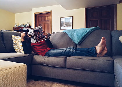 man reading book while lying on gray couch thumbnail