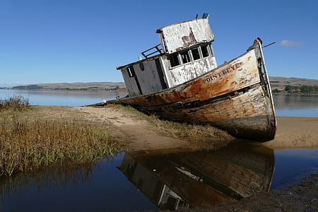 abandoned boat leaning on soil near lake during clear blue sky thumbnail