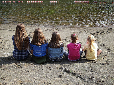 five girls sitting on seashore viewing calm sea during daytime thumbnail