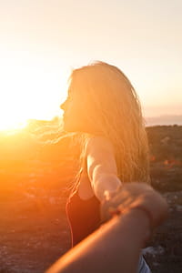 A young blonde woman looking at the sunset with her hand held by another hand thumbnail