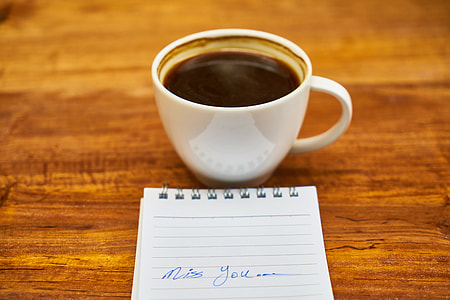 white ceramic cup beside black lined notebook on brown wooden surface thumbnail