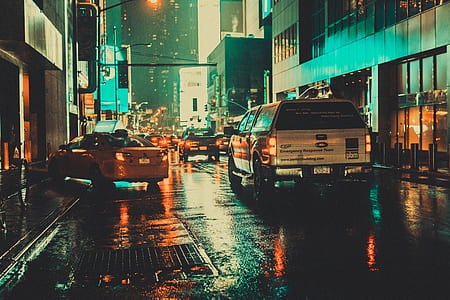 white vehicle running on wet road in between buildings at nighttime thumbnail