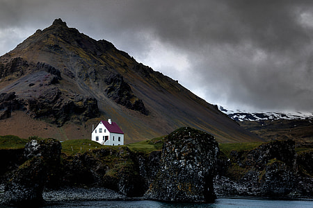alone white house on rock mountain cliff near body of water under dim sky thumbnail