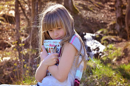 selective focus photography of girl wearing grey shirt holding book thumbnail
