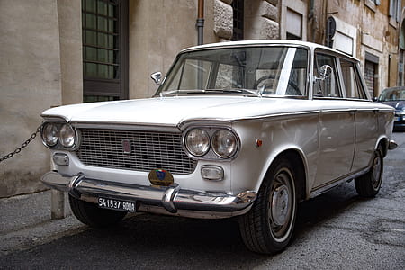classic white FIAT sedan parking beside beige concrete building thumbnail