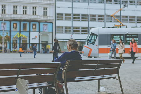 man sitting on bench while others walking near train during daytime thumbnail