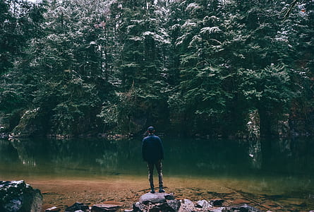 man standing on stone fronting calm body of water thumbnail