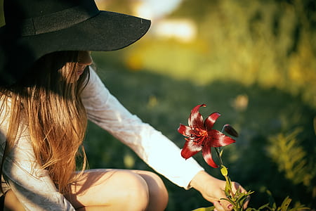 woman wearing black hat holding red lily flower at daytime thumbnail