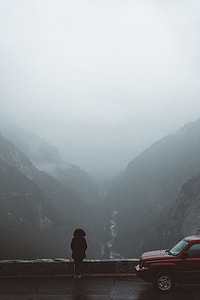 man wearing black hoodie facing cliff beside red car thumbnail