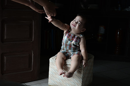 baby wearing red and gray plaid romper sitting on ottoman thumbnail