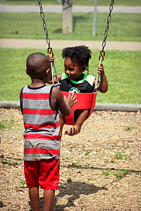 boy in red and black stripe tank top pushing red bucket swing chair thumbnail